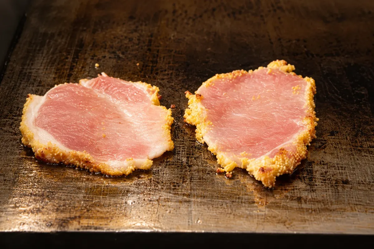 Detalle de lonjas de peameal bacon con costra de harina de maíz en la plancha.